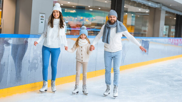happy family holding hands while skating together on ice rink
