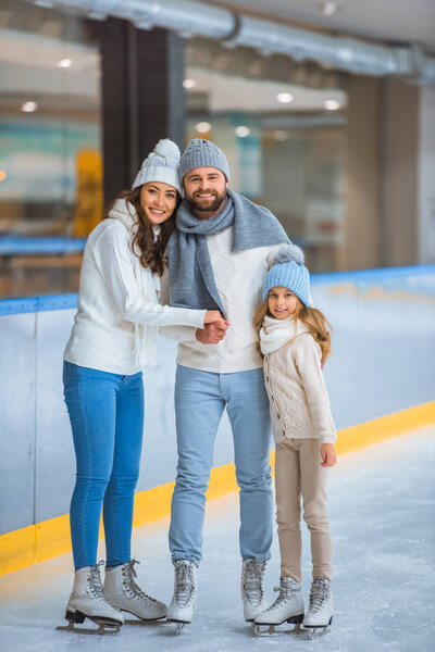 happy parents and daughter in sweaters looking at camera on skating rink