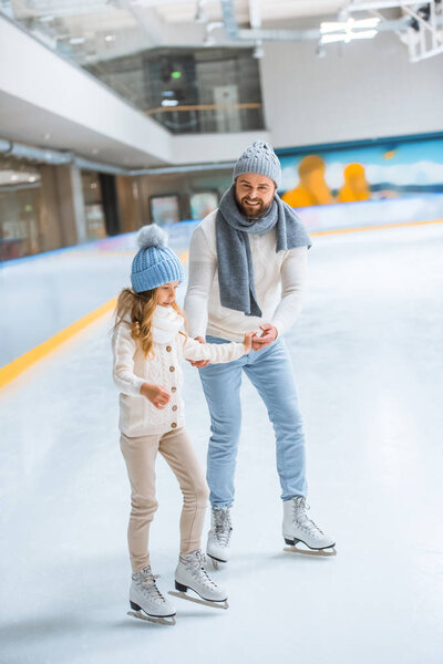 father and daughter in knitted sweaters skating on ice rink together