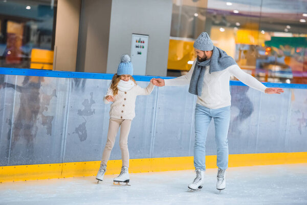 father and daughter in knitted sweaters skating on ice rink together