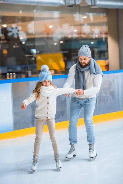 father helping little daughter to skate on ice rink