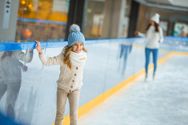 little child in knitted hat and sweater skating on ice rink