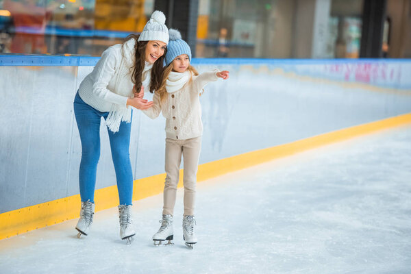 smiling daughter showing something to mother on skating rink