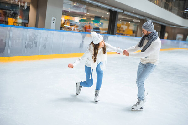 man teaching girlfriend how to skate on ice rink
