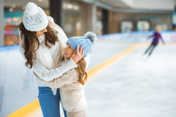 portrait of mother and daughter hugging each other while skating on ice rink together