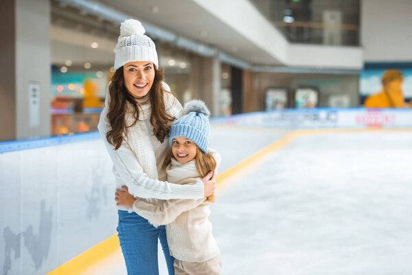 portrait of mother and daughter hugging each other while skating on ice rink together