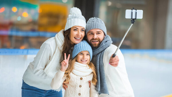 portrait of smiling family taking selfie on smartphone on skating rink