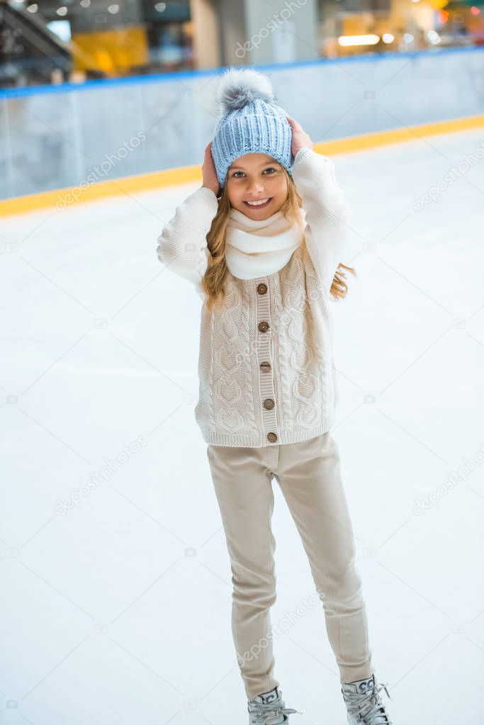 smiling adorable kid in sweater and hat on skating rink