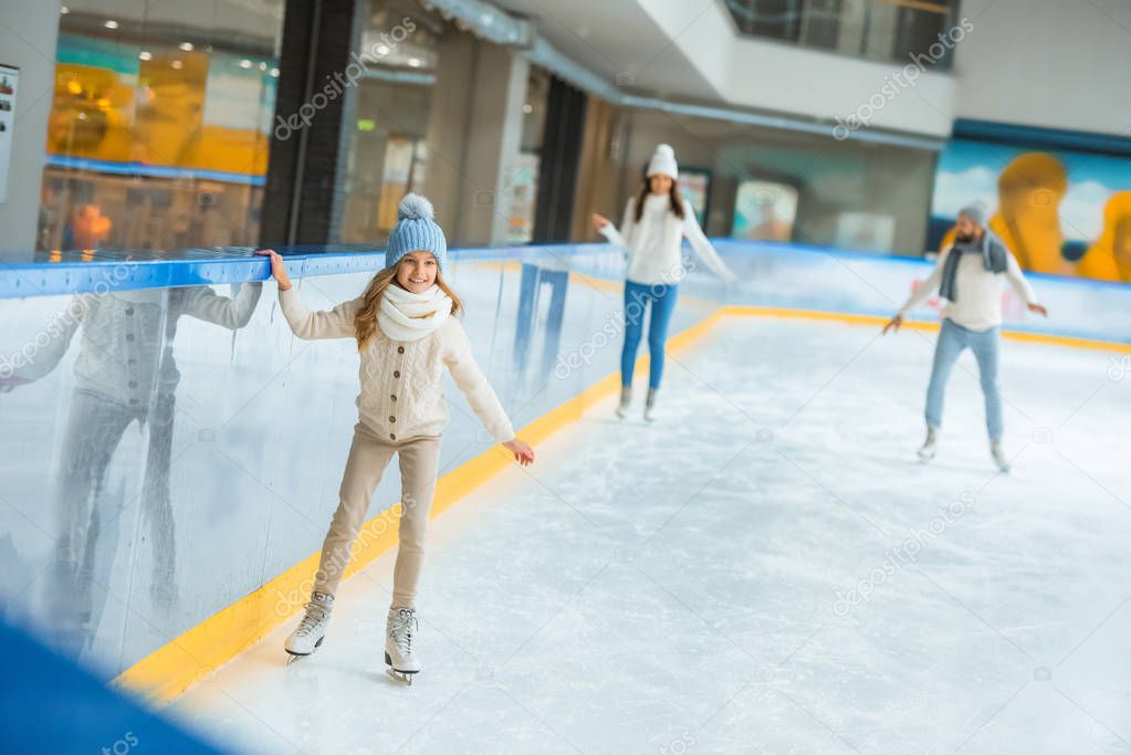 selective focus of kid skating on ice rink with parents behind