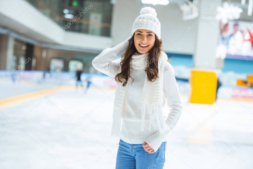 portrait of happy young woman looking at camera while skating on ice rink