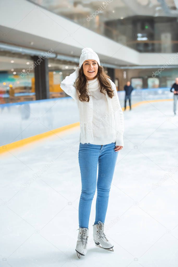 smiling young attractive woman in knitted sweater skating on ice rink alone