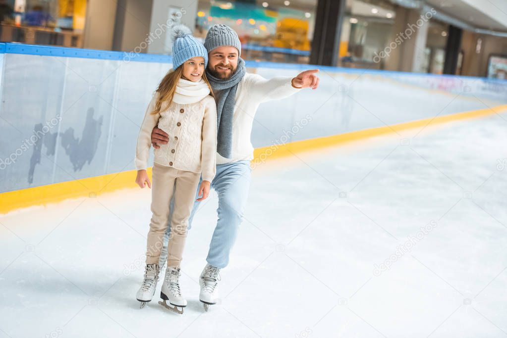 happy little daughter and father on skating rink