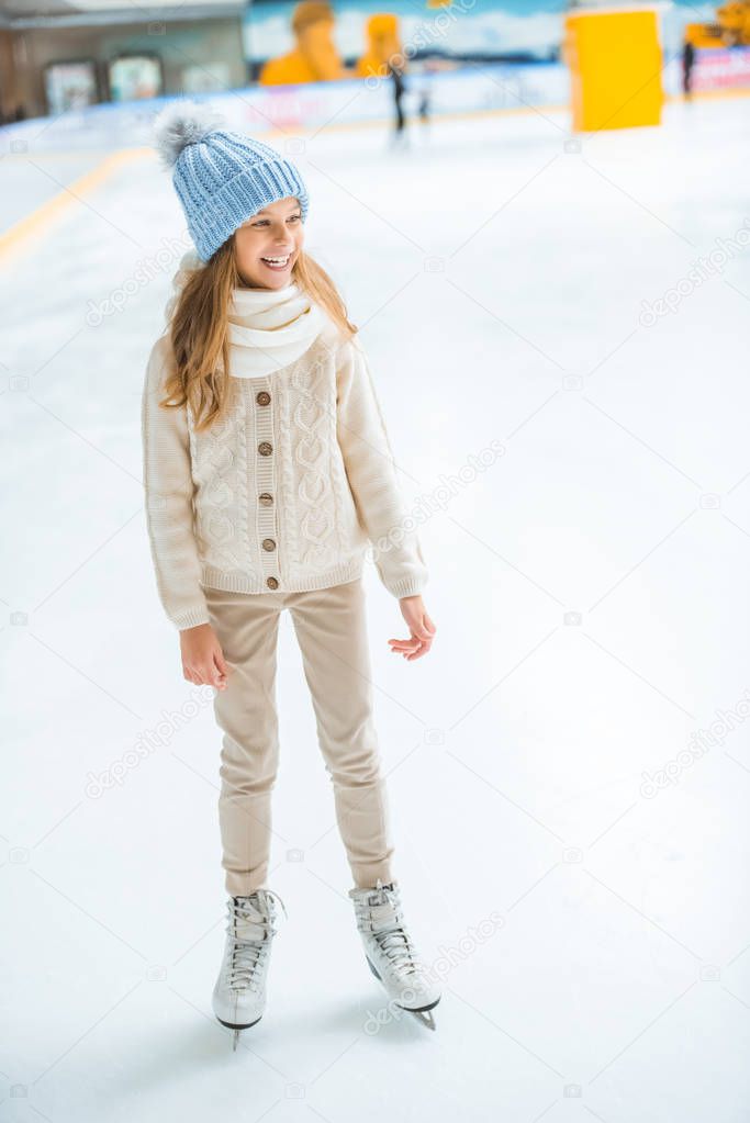 cheerful kid in sweater and skates looking away on skating rink
