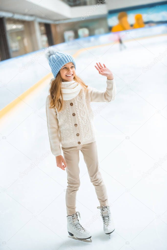 cheerful kid in sweater and skates greeting someone on skating rink