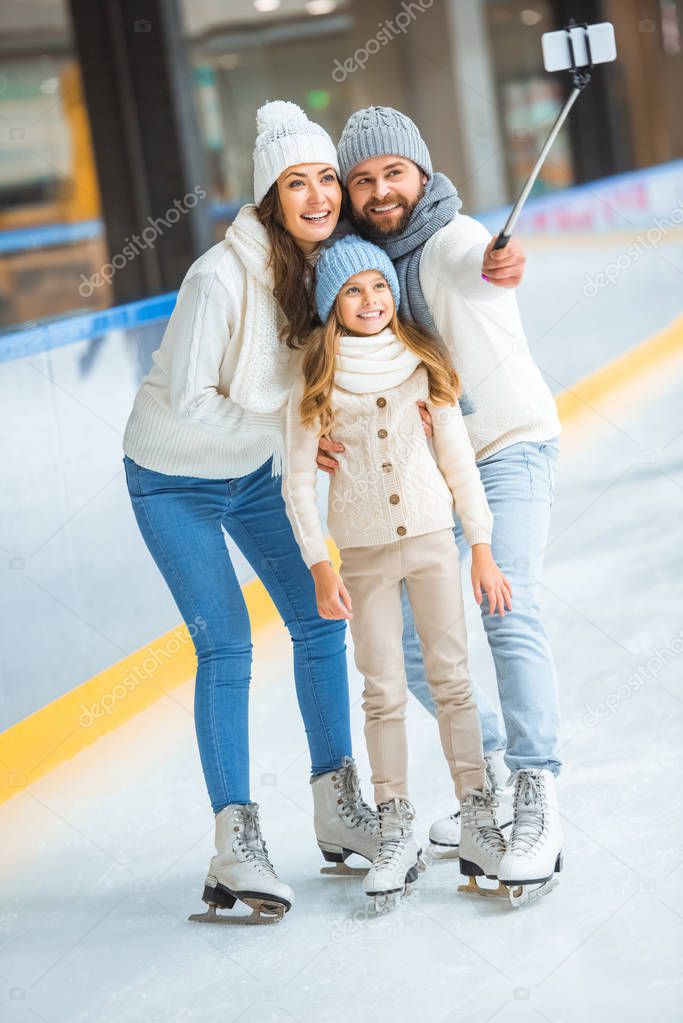 smiling family taking selfie on smartphone on skating rink