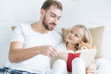 Baba ve sevimli küçük kız ayıcık yatağa birlikte kitap okuma ile 