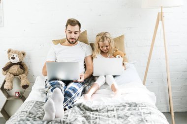 Baba ve sevimli küçük kız yatakta dizüstü bilgisayarlar kullanarak