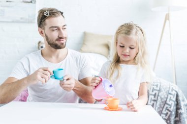 oyuncak Kupası tutarak ve küçük kızı dökme çay oyuncak su ısıtıcısı seyir gülümseyen baba
