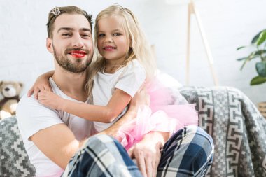 adorable little daughter in pink tutu skirt hugging happy father with red lipstick clipart
