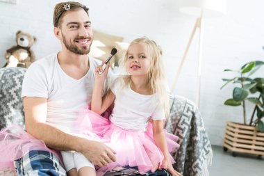 cute little child in pink tutu skirt applying makeup to happy father  clipart