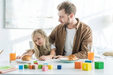 üzgün küçük kızı kruvasan kahvaltı için seyir bakarak baba