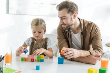 gülümseyen Baba sevimli küçük kızını evde renkli küpleri ile oynamaya bakıyor