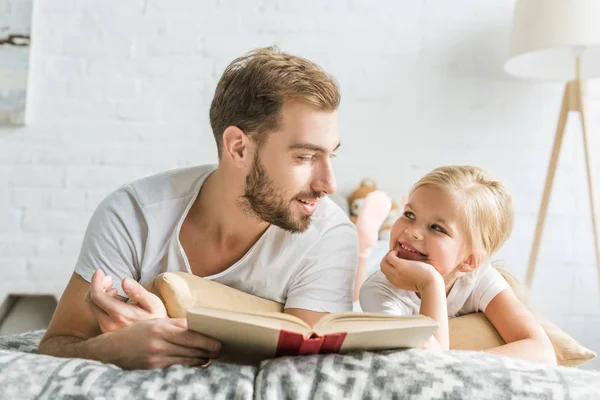 Boldog Apa Lánya Mosolyogva Minden Más Ágyon Könyv Olvasása Közben — Stock Fotó