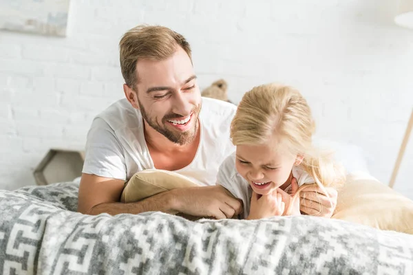 mutlu baba ve sevimli küçük kız birlikte yatakta yatarken gülüyor