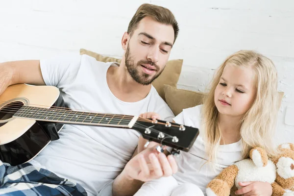 父とかわいい小さな娘のベッドの上に一緒にアコースティック ギターを演奏 — ストック写真