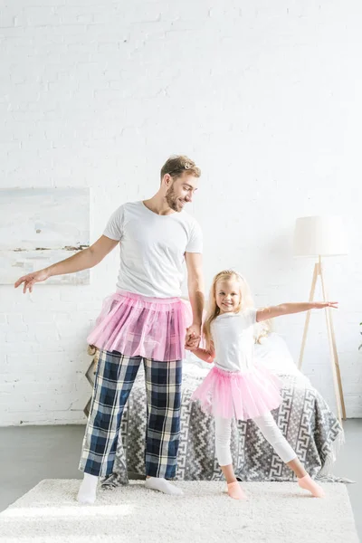 快乐的父亲和可爱的小女儿在粉红色的 Tutu 裙子手和跳舞在家里 — 免费的图库照片