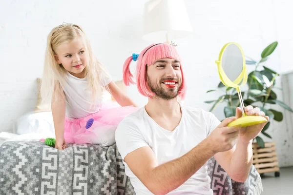 sevimli küçük kızı tutu etek ve pembe peruk aynaya bakarak içinde gülümseyen baba  