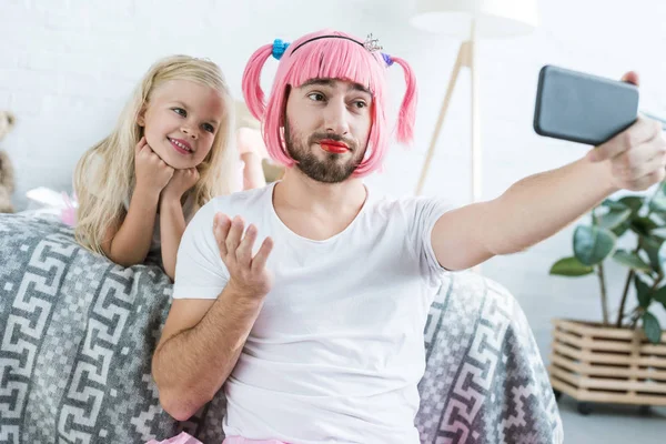 快乐的小女儿和父亲在粉红色的假发采取自拍与智能手机在家里 — 图库照片