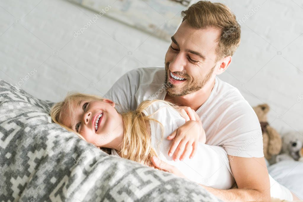 Happy father hugging adorable little daughter on bed