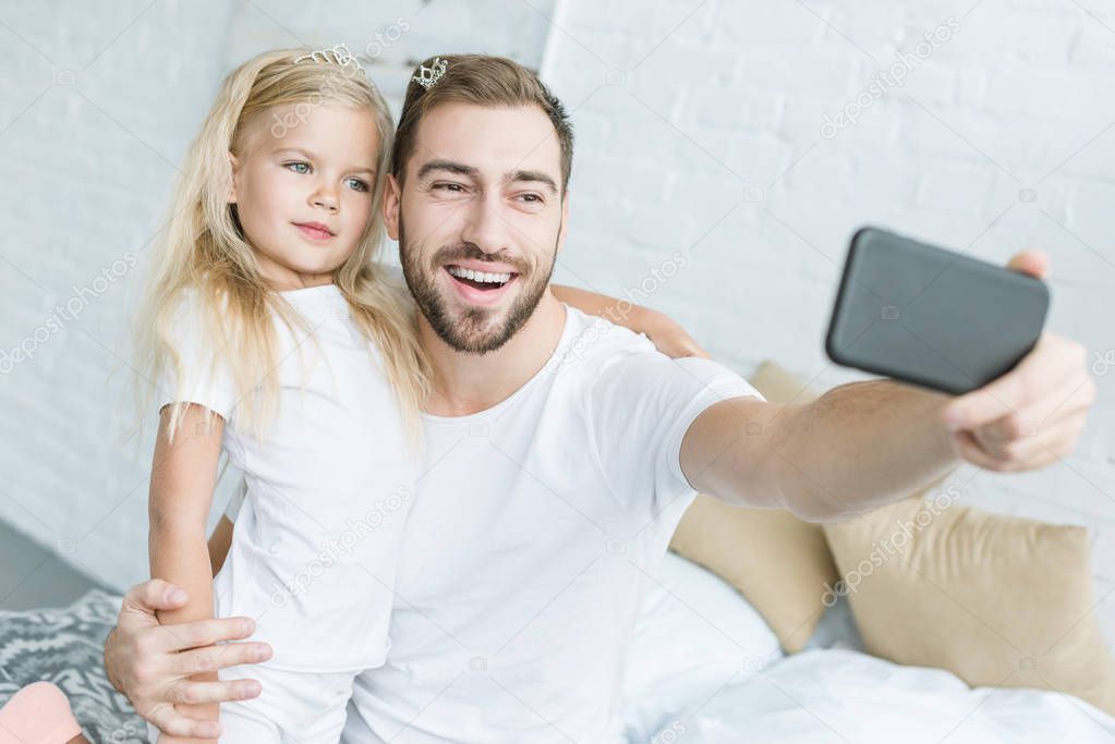 happy father and cute little daughter taking selfie with smartphone at home