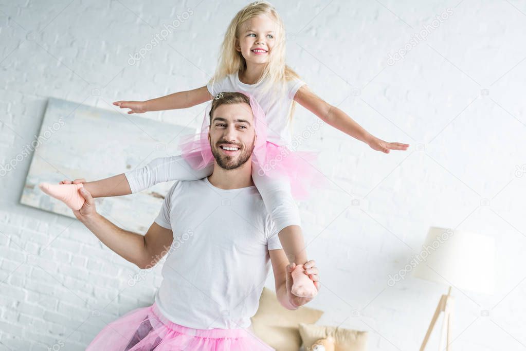 happy father in pink tutu skirt carrying adorable smiling daughter on neck 