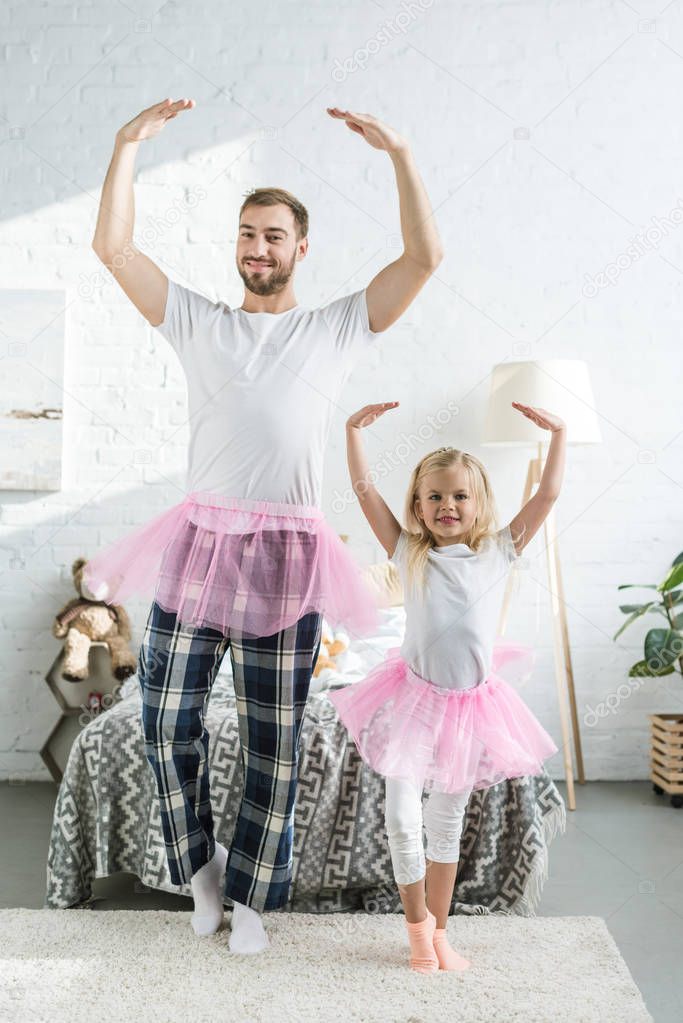 happy father and adorable little daughter in pink tutu skirts dancing and smiling at camera