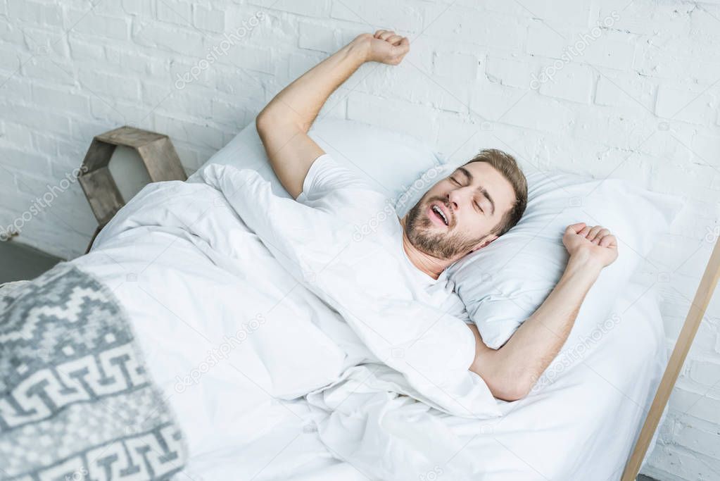 high angle view young man yawning and stretching in bed 