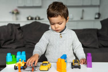 oyuncak arabalar ve plastik bloklarıyla evde oturma odasında masasında oynayan çocuk, seçici odak