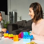 Gelukkig moeder en zoontje spelen met kleurrijke kunststof blokken thuis