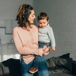 Hermosa mujer sosteniendo adorable niño en las manos en casa