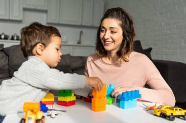 Anne ve küçük oğlu renkli plastik blokları ile evde oynarken gülümseyen