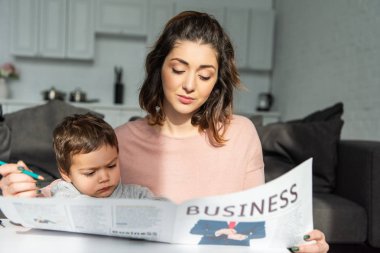 Anne ve küçük oğlu evde oturma odasında iş gazete okuyan seçici odak