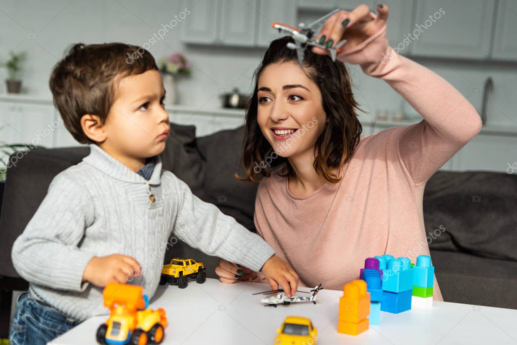 Positive woman playing with toy airplane near little son at home