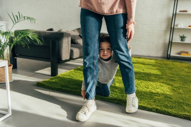 little boy sitting between mother legs in living room at home