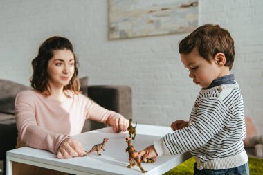 Anne ve küçük oğlu toy dinozorlar evde oturma odasında masada oynarken seçici odak