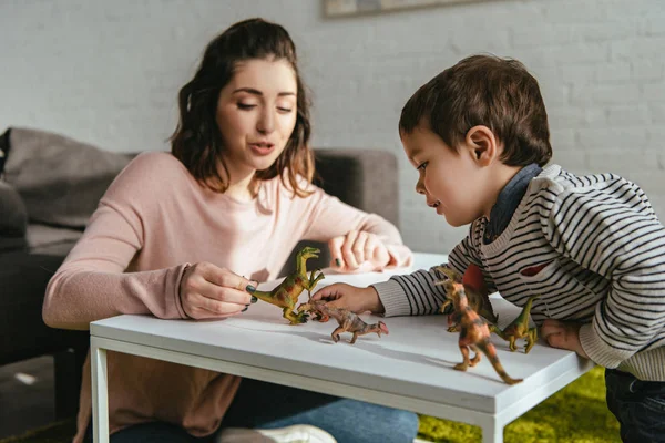 Gladlynt Kvinna Och Lille Son Spelar Toy Dinosaurier Bord Vardagsrummet — Gratis stockfoto