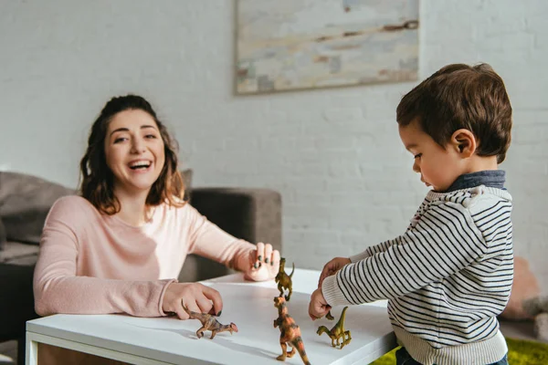 Skrattande Kvinna Och Lille Son Spelar Toy Dinosaurier Bord Vardagsrummet — Stockfoto