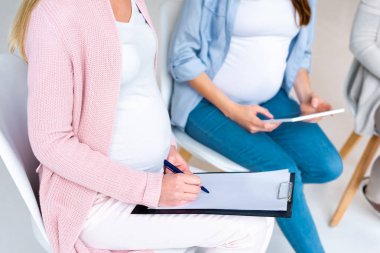 cropped view of pregnant women filling form and using digital tablet at prenatal class isolated on grey clipart