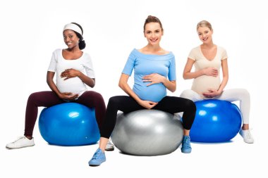 Beyaz arka plan üzerinde izole fitness topları oturan üç hamile kadınlar