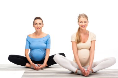 two pregnant women sitting on floor and holding hands on feet isolated on white clipart